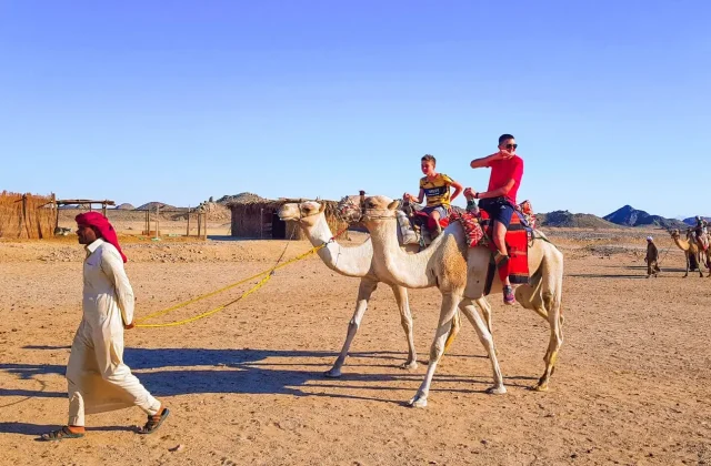 Guide leading a camel with two riders through a desert village