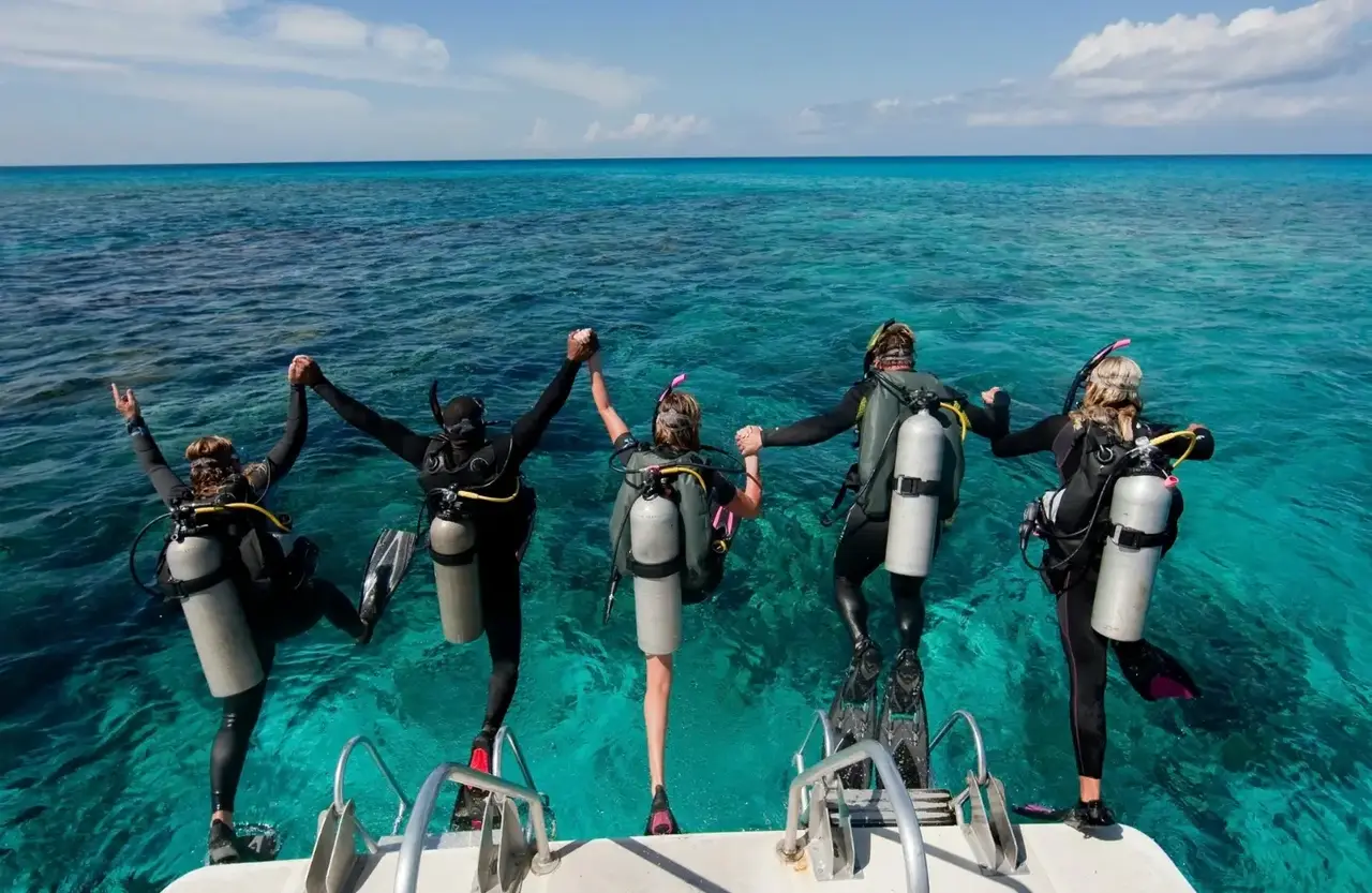Group of divers in full gear holding hands on the back of a boat