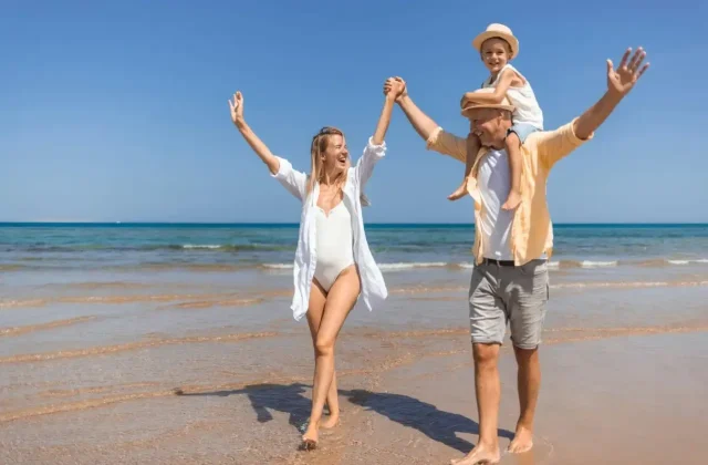 Family cheering with arms raised on a sandy beach on a sunny day