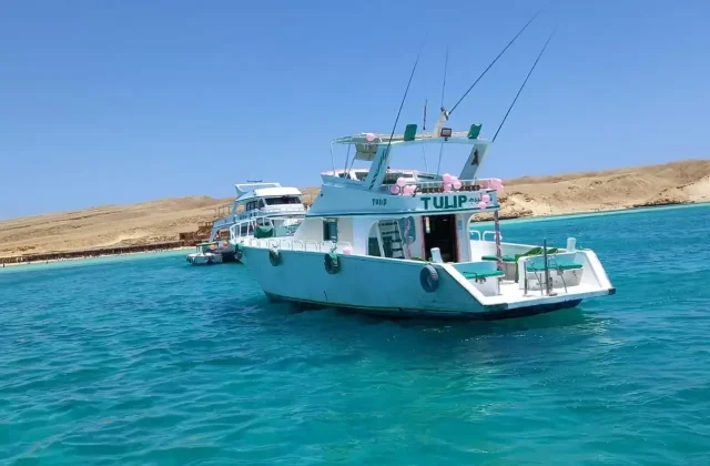 White fishing boat with rods anchored in turquoise water near a desert island