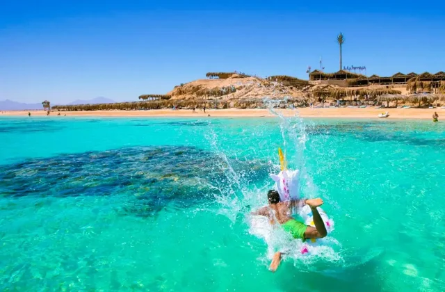 Swimmer splashing into turquoise water off a sandy Red Sea island beach with shade huts