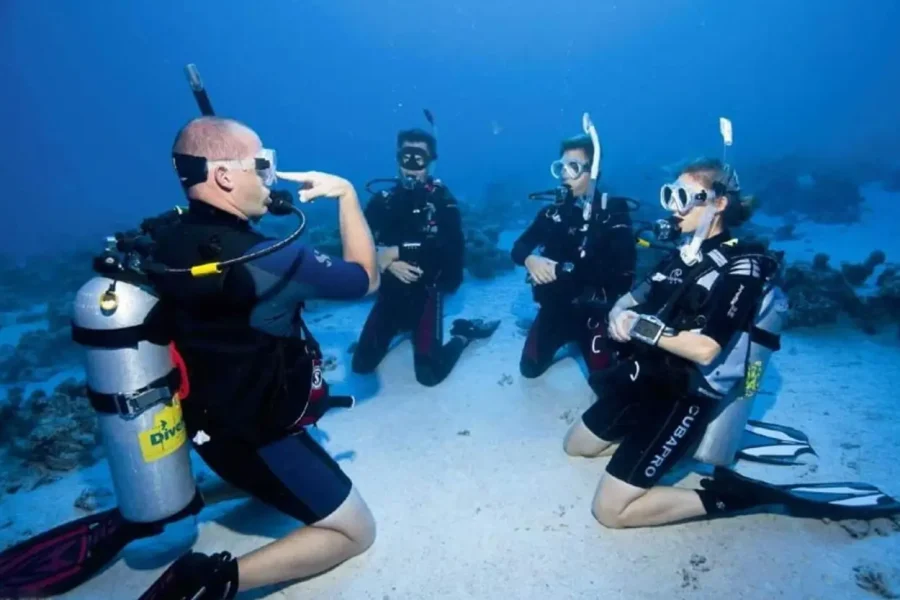 PADI-Tauchlehrer erklärt Schülern am sandigen Meeresboden den Ablauf
