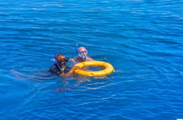 Snorkelers holding a yellow ring float at the surface of the blue sea