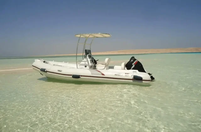 Small white speedboat anchored in very shallow turquoise water off a sandy island