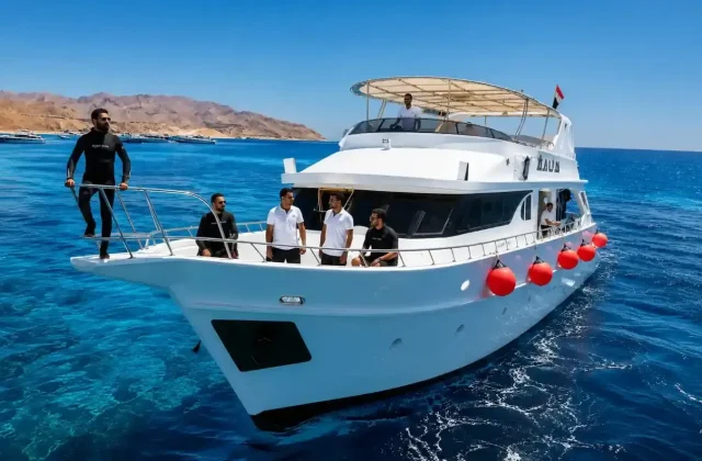 White private boat with crew standing on the bow on deep blue water, desert mountains behind